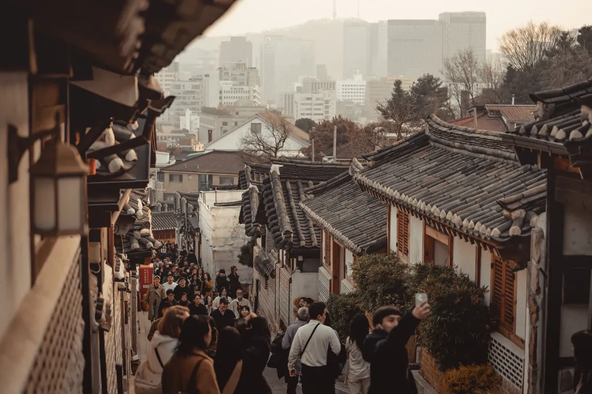 Explore the vibrant atmosphere of Bukchon Hanok Village in Seoul as tourists stroll past traditional Korean architecture.