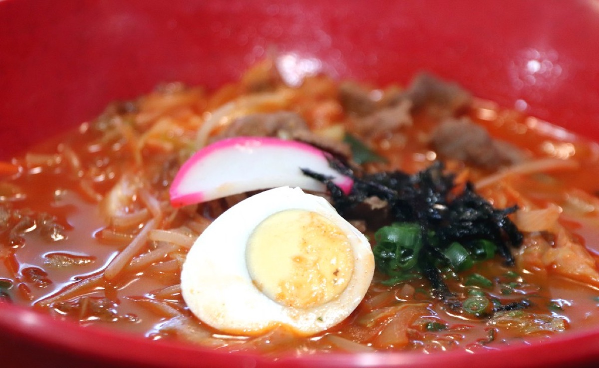 A steaming bowl of spicy Korean instant noodles with red sauce.
