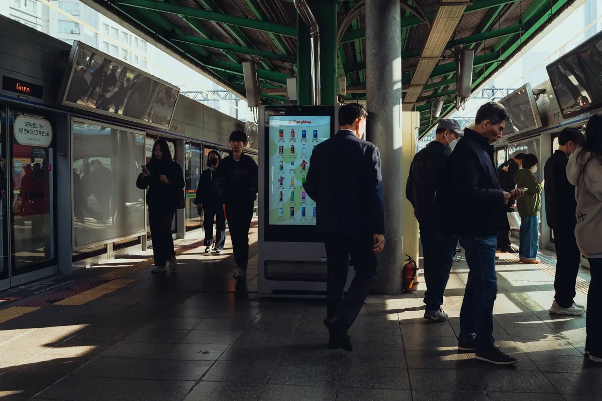 Commuters at a bustling Seoul subway station platform during the day.