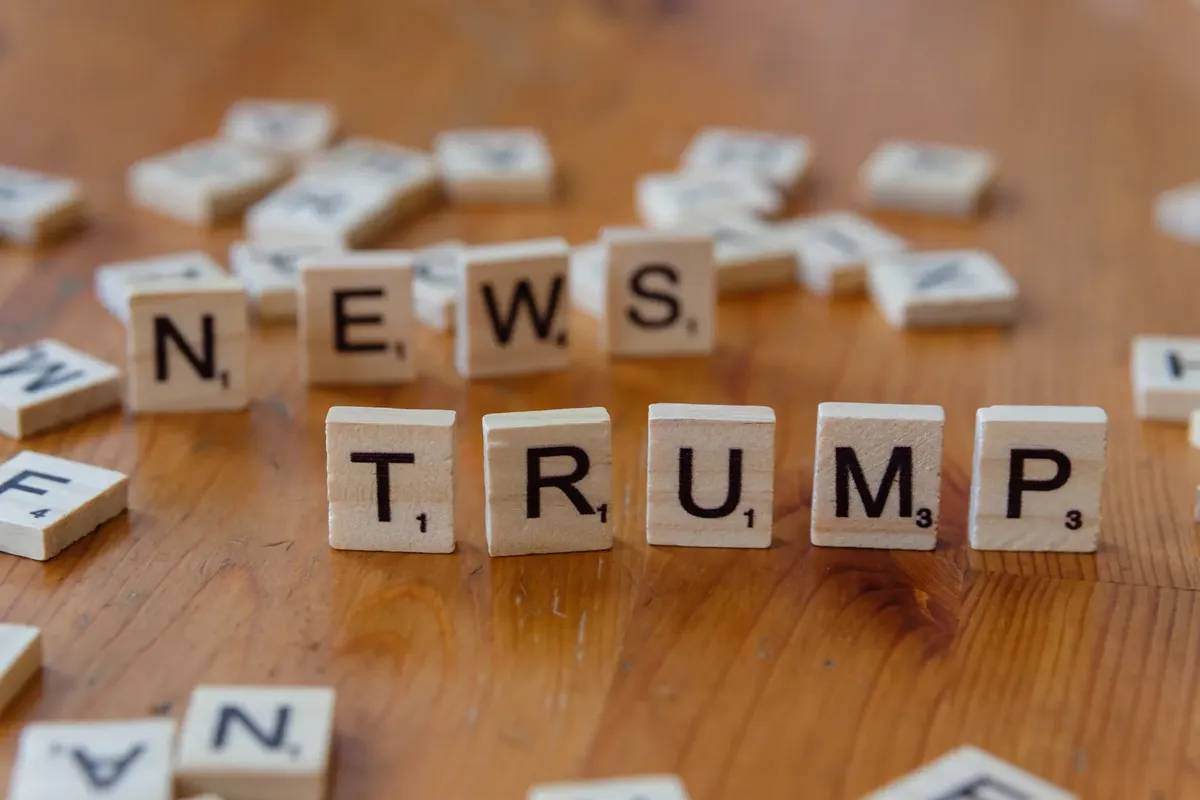 목재 테이블 위에 'NEWS'와 'TRUMP'라는 글자가 목재 레터타일로 구성되어 있으며, 정치적 논의와 관련이 있다.
