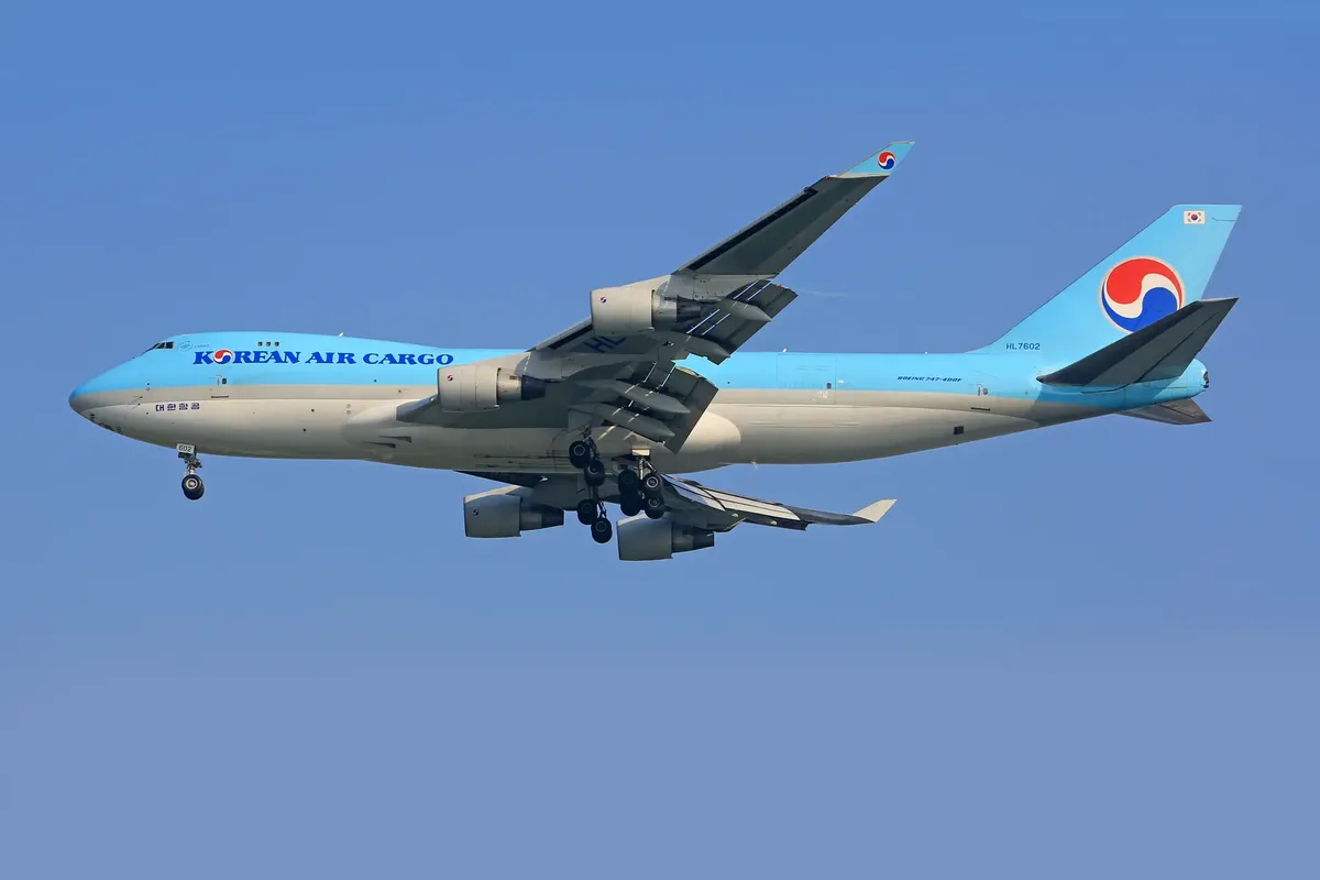 A Korean Air Cargo airplane flying in the clear blue sky, featuring a white and blue design.