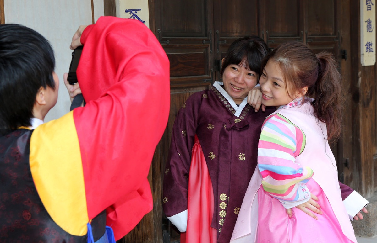 A person wearing a traditional Korean hanbok standing in a historical Korean village