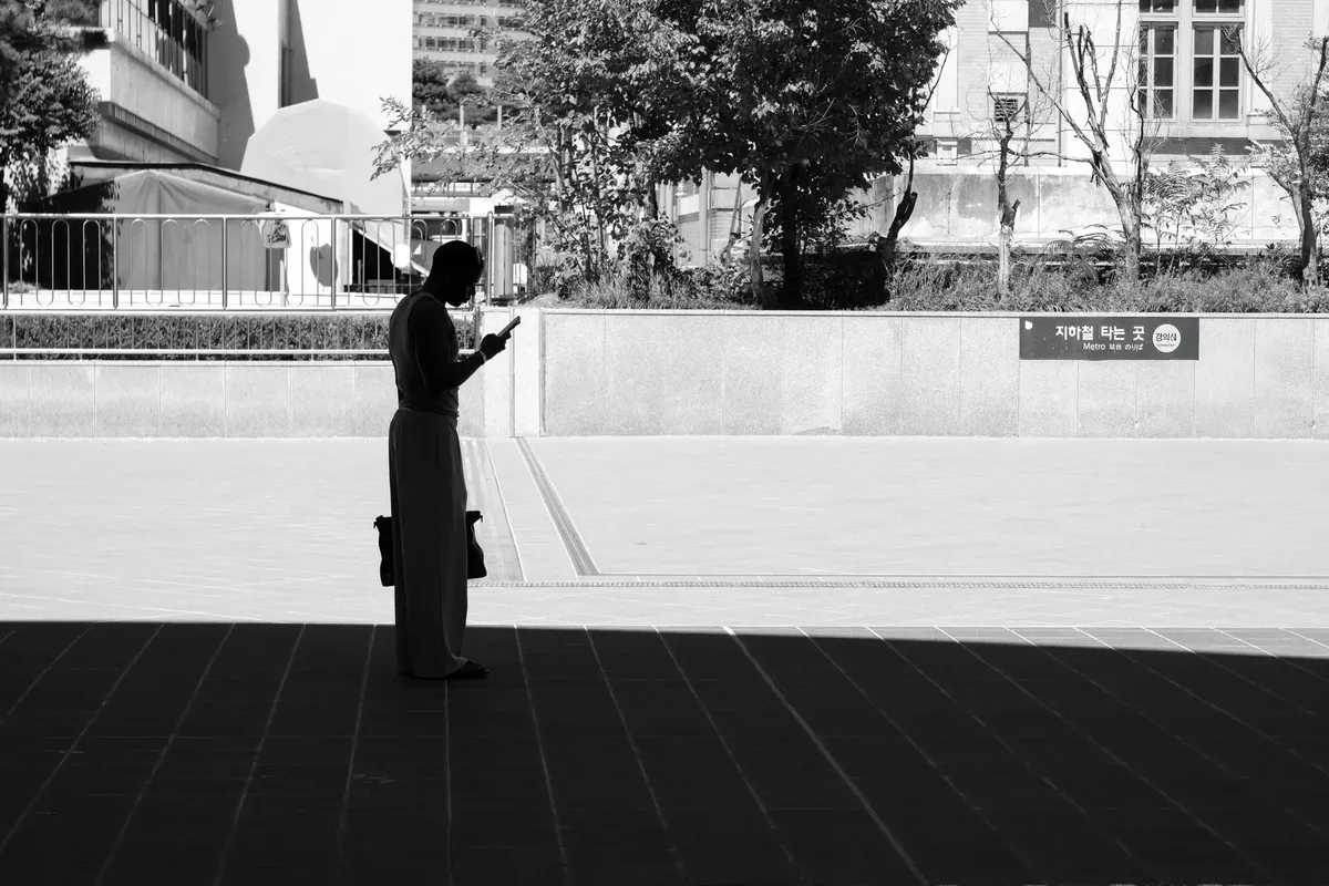 Black and white silhouette of a person using a smartphone in an urban outdoor setting.