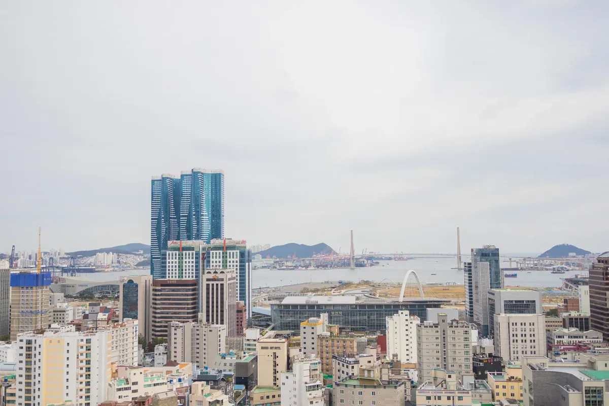 Aerial view of Busan, South Korea, featuring modern skyscrapers and coastline on an overcast day.